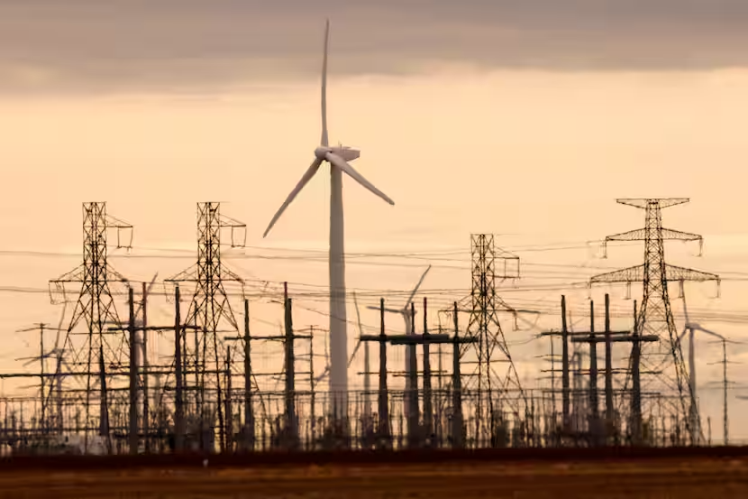 Wind turbine behind a substation and transmission towers under a hazy orange sky